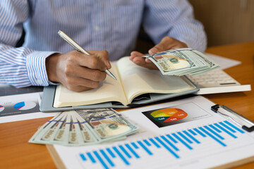 Close-up businessman holding banknotes counting money and writing notes on notepad. Accounting Concepts and Personal Financial Planning