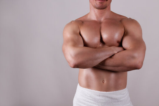 Professional bodybuilder wearing just a towel posing over isolated grey background. Studio shot of a shirtless fit guy flexing the muscles. Close up, copy space.