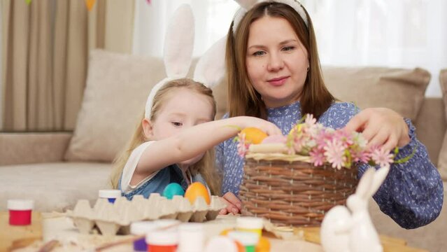 mom and little daughter with rabbit ears celebrate Easter and lay painted eggs 
