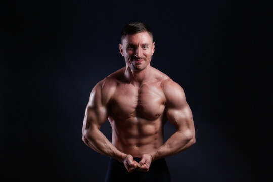 Professional bodybuilder posing over isolated black background. Studio shot of a fitness trainer flexing the muscles. Close up, copy space.