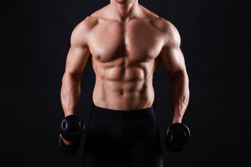 Professional bodybuilder performing exercise with dumbbells over isolated black background. Studio shot of a male fitness model pumping iron. Close up, copy space.