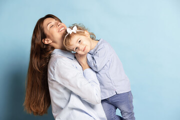 Studio shot of beautiful happy woman and little kid, mother and daughter isolated on blue background. Mother's Day celebration. Concept of family, childhood