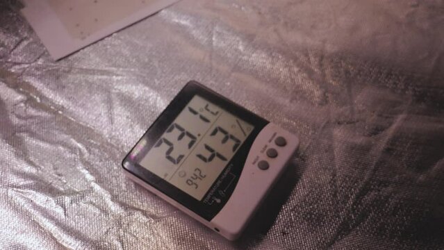 Digital thermometer humidity meter placed on the floor of a reflective grow tent for indoor growing DIY farming with LED