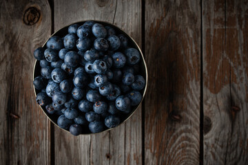 Bowl of fresh blueberries on rustic wooden table with copy space.
