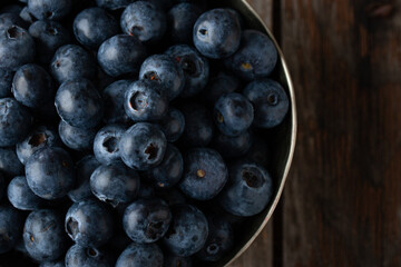 Bowl of fresh blueberries on rustic wooden table with copy space.