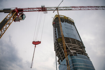 Skycraper under construction. Huge modern building work in progress with enormous crane in first...