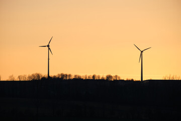 Silhouettes of two wind wheels in front of a beautiful sunset. Renewable electricity generation with wind turbines.