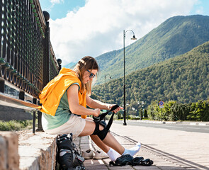 Young woman in yellow hoodie putting on protective equipment before roller skating on embankment...