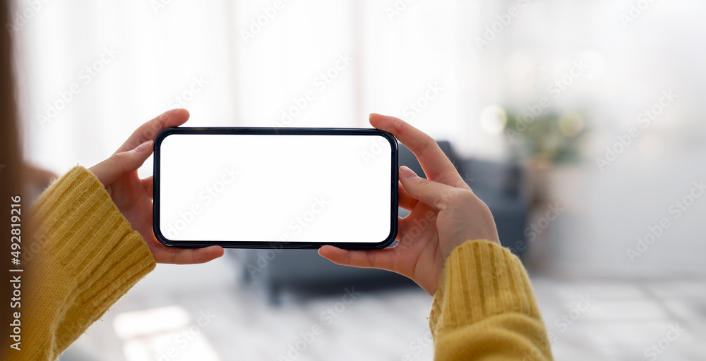 Poster mockup image of a woman holding and using mobile phone with blank desktop screen in horizontal view.
