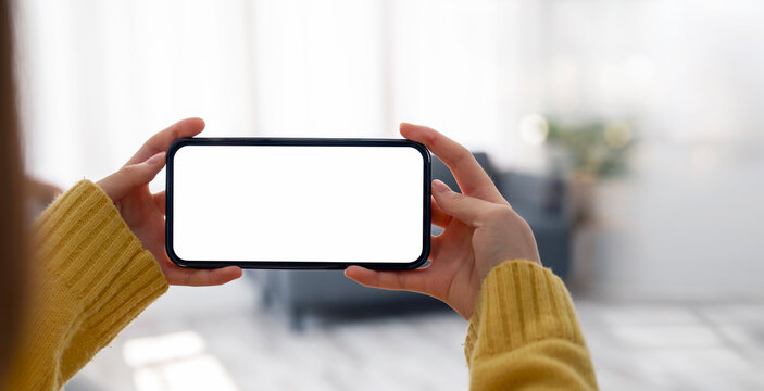 Mockup image of a woman holding and using mobile phone with blank desktop screen in horizontal view.