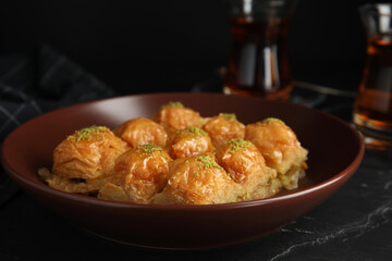 Delicious sweet baklava in bowl on black table, closeup