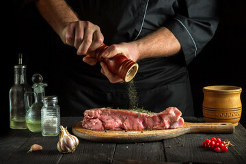 The chef prepares raw veal meat. Before baking, the chef adds pepper to the beef. National dish is being prepared in the kitchen