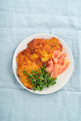 Potato pancakes. Fried homemade potato pancakes or latkes with cream, green onions, microgreens, red salmon and sauce in rustic plate on blue linen tablecloth. Rustic style. Healthy food. Top view.