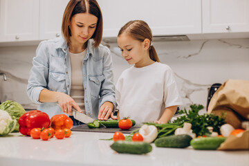 Mother with daughter preparing dinner from fresh vegetables at the kitchen