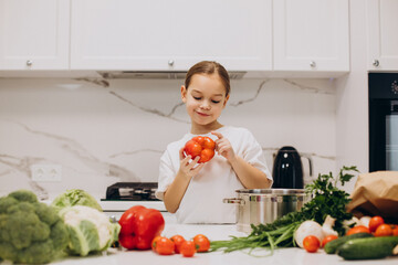 Little girl preparing salad at home at kitchen