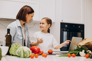 Mother with daughter preparing dinner from fresh vegetables at the kitchen