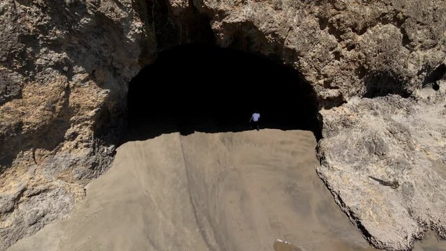 Downward aerial shot of Bethells Beach with a man walking into the cave