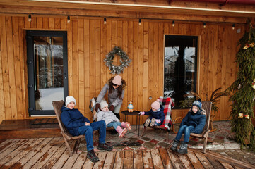 Attractive mother with her four kids on the terrace of a wooden house  in winter day.