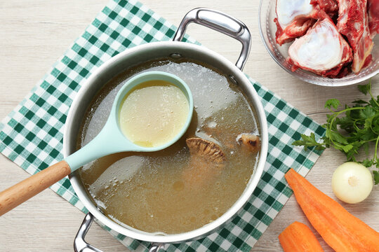 Delicious homemade bone broth and ingredients on white wooden table, flat lay