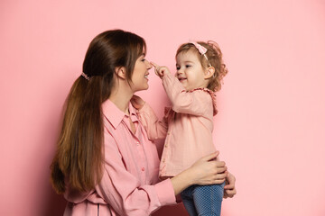 Happy woman and little girl, caring mother and daughter isolated on pink studio background. Mother's Day celebration. Concept of family, childhood, motherhood - obrazy, fototapety, plakaty
