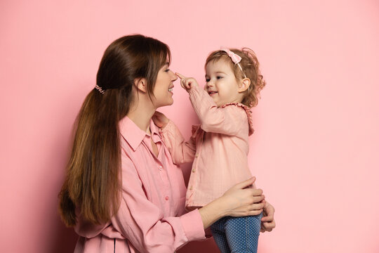 Happy woman and little girl, caring mother and daughter isolated on pink studio background. Mother's Day celebration. Concept of family, childhood, motherhood