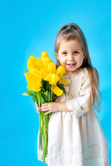 Obraz na płótnie Canvas portrait of a smiling little girl a child with a bouquet of yellow tulips on a blue isolated background. Lifestyle. International Women's or Mother's Day. Space for text. High-quality photography