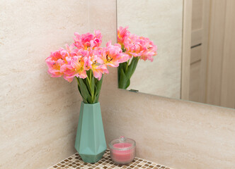fresh pink tulips in vase and candle on bathroom countertop with mirror reflection. home decoration