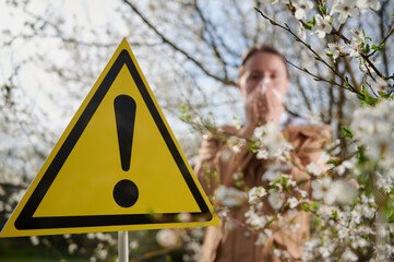 Attention sign. Woman allergic suffering from seasonal allergy at spring, posing in blossoming...