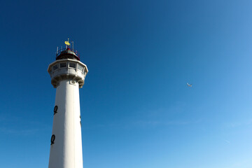 White lighthouse and white airplane in blue sky on sunny day.