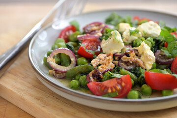 Salad from green beans, peas and tomatoes, with braised onions and feta cheese, healthy vegetarian meal for a ketogenic or low carb diet, close-up, selected focus