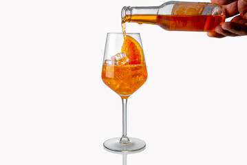 Alcoholic Aperol Spritz Cocktail poured from glass bottle into glass with ice cube and orange...
