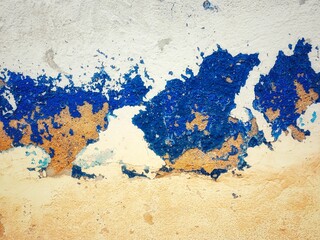 surface of the old cement wall is painted white and blue, peeling off and cracking.