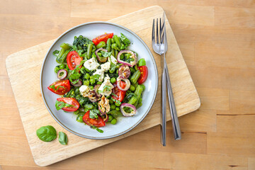 Vegetable meal from green beans, peas, and spinach with braised onions, feta cheese and tomatoes for a vegetarian low carb diet on a wooden table, copy space, top view from above