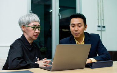 Fototapeta premium Senior aging businesswoman and young adult handsome smart businessman working overtime together at night, using laptop for creative project marketing plan, smiling with confidence and happiness.