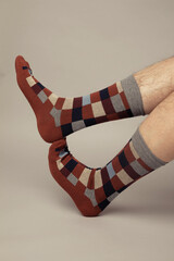 Studio photo of a caucasian's man's feet wearing colourful checkered socks. The background is grey.
