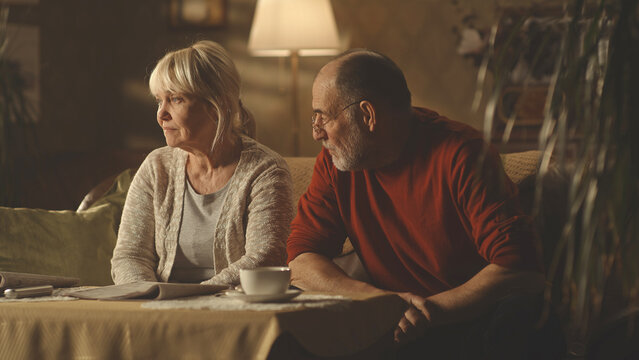 Irritated aged husband blaming upset wife while sitting on sofa at home together