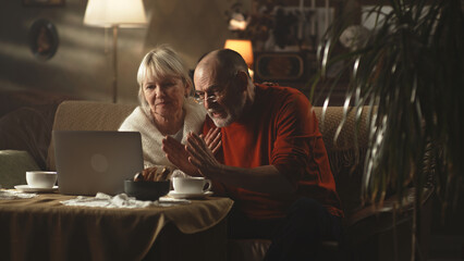Aggressive man having argument with kids online, while sitting on sofa near woman and making video call via netbook laptop in cozy living room at home