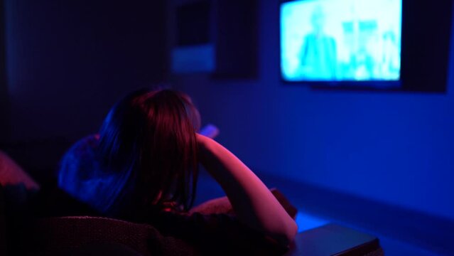  girl sitting on a sofa watching a movie on TV.