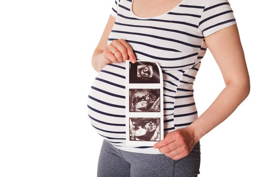 Pregnant woman standing and holding her ultrasound baby scan picture isolated on white