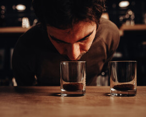 The barista chooses coffee varieties for the coffee shop by smell - he sniffs the ground beans in a glass with his nose