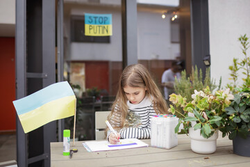 Small Ukrainian girl draws blue and yellow national flag in safe place abroad in Europe where she...