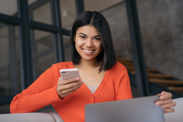 Portrait of beautiful confident businesswoman using laptop computer holding mobile phone sitting in...