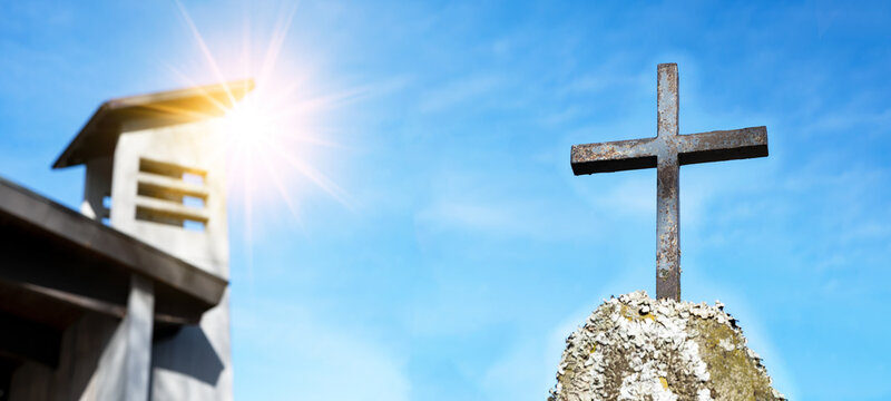 Religious Background - Blue sky with old weathered cross on rock on cemetery or church, illuminated by the sun