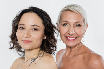 Smiling senior woman with naked shoulders near friend isolated on grey, feminism concept.