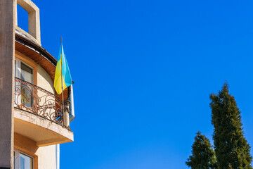 Fototapeta na wymiar Flag of Ukraine on the balcony of the house against the blue sky on a sunny day. Bottom view