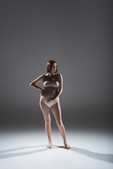 Pregnant woman in underwear touching belly on grey background