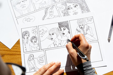 The artist draws a storyboard of comic book characters on sheets of paper. - 492837884