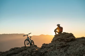 Gordijnen Cyclist mtb biker sits and relax on mountain top at sunset © cppzone