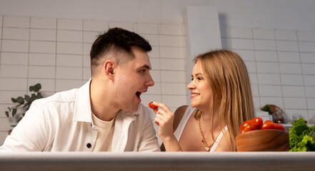 Happy couple cooking at home. Beautiful woman feeding handsome man tomato. Romantic and tender relationship. High quality photo