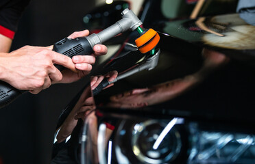 Close up of car detailist hands, cleaning or pilishing the car by poliermaschine, car detailing concept, orbital polisher in repair shop polishing car